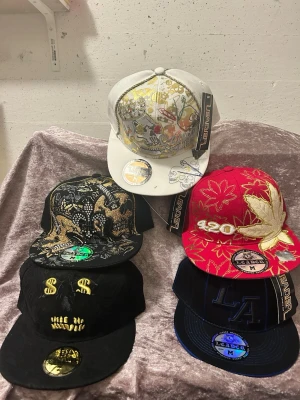 Färgglada snapbacks med brodyr - Säljer flera snapback-kepsar i olika färger och mönster, bland annat med broderade motiv som blad, dollar-tecken, LA och NY-loggor. Kepsarna har platt skärm och justerbar passform. Perfekt för dig som vill sticka ut med din stil. 145kr/st , helt ny 