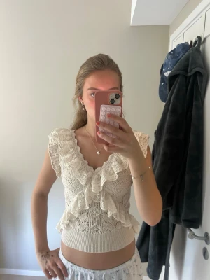 Beige stickad volangtopp - Supersöt beige stickad topp med volangdetaljer och v-ringning från Zara. Toppen är ärmlös och har en croppad passform som ger en trendig look. Perfekt att styla med höga jeans eller kjol för en fräsch sommarstil. Är egentligen i storlek L men skulle säga att den sitter mer som en S/M