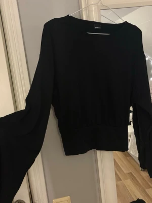 Svart topp med vida ärmar - Svart topp från Gina Tricot med bred resår i midjan och långa, vida ärmar. Knappt använd. Mjuk o skön. Säljer för 150kr + frakt