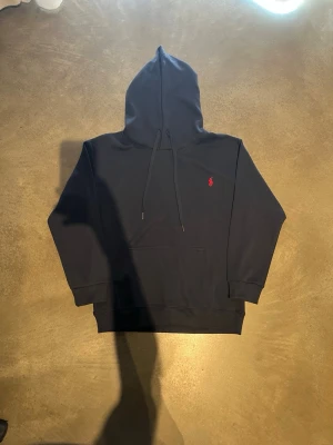 Mörkblå hoodie  - Snygg mörkblå hoodie med klassisk röd logga broderad på bröstet. Hoodien haranvänts ett fåtal gånger med varsamhet. Perfekt för en chill och stilren look. Pris kan diskuteras. Hör av er vid frågor!😊