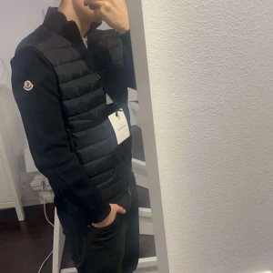 Moncler Cardigan - Snygg svart dunväst från Moncler med ett stilrent och quiltat mönster. Västen har en dragkedja framtill och är perfekt för lager-på-lager under kyligare dagar. Den ikoniska Moncler-loggan syns på armen. Kan sänka priset lite vid snabb affär 