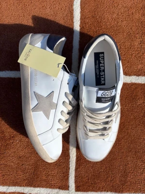 Golden Goose Super-Star💫 - Säljer dessa då jag missade returtiden och inte fick returen godkänd av deras kundtjänst😅. De är 100% oanvända och bara uppackade för bilderna🧼📸! Vit bas med grå mockastjärna och marinblå häl🤍🩶💙. Passar till allt! 👖👟                      Storlek: 42                                                ㅤㅤ ㅤ100% nyskick / Oanvända 💎ㅤㅤㅤㅤㅤㅤㅤㅤㅤIngår: Originalbox, dustbag & alla tillbehör 🎁                                                  Skickas snabbt och spårbart! 📦💨ㅤ       ㅤㅤㅤㅤSkriv i DM vid frågor! 👋🤝💌