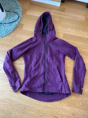 Lila hoodie från Nike med dragkedja - Snygg lila hoodie från Nike med hel dragkedja framtill och två fickor. Hoodien har en sportig passform, huva med dragsko och är tillverkad i mjukt bomullsmaterial. Perfekt för en avslappnad och trendig stil. XS