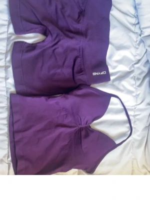 Lila seamless set från DFYNE - Säljer ett lila seamless set från DFYNE med ett linne med smala axelband och matchande shorts. Setet är stretchigt och sitter skönt mot kroppen, perfekt för en sportig och trendig look. Materialet är mjukt och följsamt.
