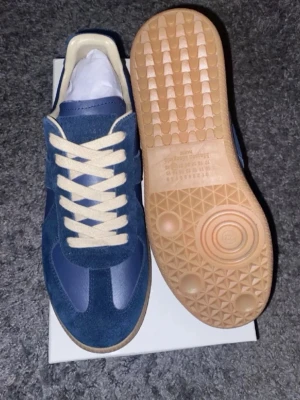 Maison Margiella ”gats” - Snygga blå sneakers med beige detaljer och gummisula. DEM ÄR ANVÄNDA OCH ÄR BEGAGNADE, SKOR MEDFÖLJER ENBART FRÅN BILDEN OCH EJ ORIGINAL SKORKARTONG! Pris kan diskuteras vid snabbaffär.