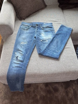 Blå slitna jeans med skinny fit - Snygga blå jeans med skinny fit och slitna detaljer på benen. Jeansen har en klassisk femficksdesign, ljusa tvättade partier och coola hål samt färgstänk för en trendig look. Perfekta för dig som gillar en avslappnad och modern stil.