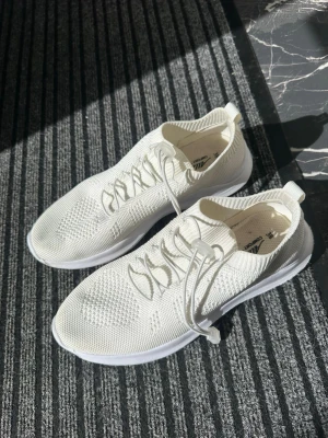 Vita stickade sneakers med snabbsnörning - Snygga helvita sneakers med stickad ovandel och elastisk snabbsnörning. Skorna har en sportig och modern look med låg profil och ventilerande meshmaterial. Perfekta för dig som gillar stilrena och bekväma sneakers till vardags.