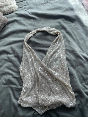 Glittrig festtop - Snygg glittrig halterneck topp i silver med omlott-design och djup v-ringning. Knappt använd🥰