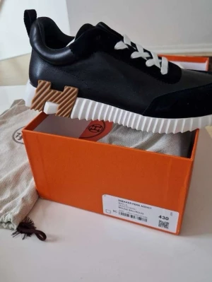 Svarta H sneakers - Snygga svarta H sneakers med vit, räfflad sula och vita skosnören. Skorna har detaljer i mocka och läder samt en unik H-detalj på sidan av sulan. Perfekta för dig som vill ha något exklusivt och trendigt i garderoben.