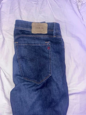 Mörkblå jeans från Replay - Snygga mörkblå jeans från Replay med klassisk femficksdesign och detaljer som Replay-logga på bakfickan och metallmärke fram. Jeansen har raka ben och är tillverkade i ett mjukt denimtyg som sitter skönt. Perfekta för en trendig och avslappnad look.