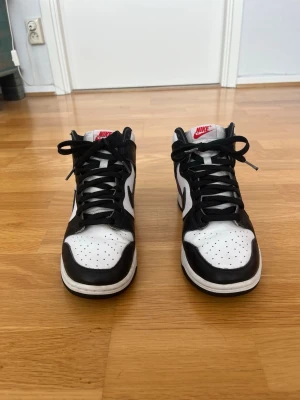 Nike Dunk High Panda sneakers - Storlek 40 - Säljer ett par stilrena Nike Dunk High i den populära svartvita Panda-färgen. Skorna är i bra skick med normala tecken på användning och har fortfarande mycket kvar att ge. Passar perfekt både till vardag och streetwear. Bekväma på foten och enkla att matcha med olika outfits. Storlek EU 40.