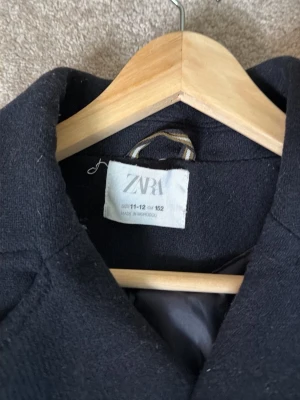 Mörkblå dubbelknäppt rock från Zara - Stilren mörkblå rock från Zara med dubbelknäppning och bred krage. Rocken har två raka fickor framtill och en klassisk, rak passform. Tillverkad i ett tjockare tyg som passar perfekt för kyligare dagar.