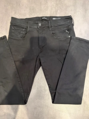 Svarta jeans från Replay  - Svarta slim fit jeans från Replay, modell Anbass. Klassisk femficksdesign med snygga detaljer och logotyp på fickan. Jeansen har en modern passform och är tillverkade i stretchigt material för extra komfort.