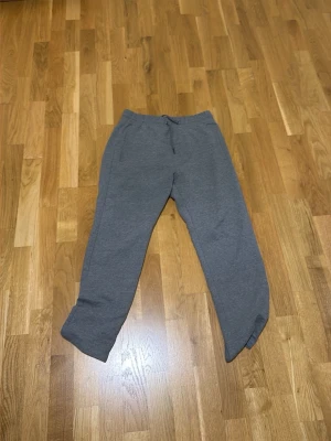 Grå mjukisbyxor med dragsko - Ett par grå mjukisbyxor med rak passform och dragsko i midjan. Byxorna har sidofickor och är tillverkade i ett mjukt och bekvämt material, perfekt för chill dagar. Enkel design utan synligt märke.