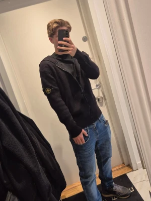 Svart kofta från Stone Island -cardigan - Svart stickad hoodie från Stone Island med dragkedja framtill och den klassiska logopatchen på vänster ärm.                               Storlek: M (Passar även S)                                Skick: 10/10
