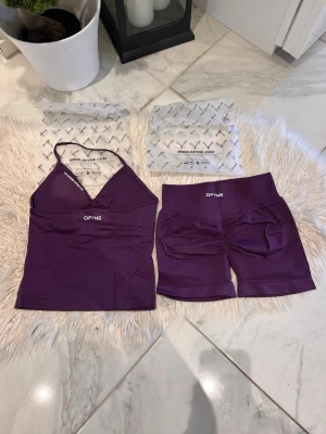 Slutsåld färg DFYNE - Säljer ett snyggt lila träningsset från DFYNE med ett linne med smala axelband och matchande shorts med hög midja. Materialet är stretchigt och följsamt, perfekt för gym eller yoga. Båda plaggen har DFYNE-logga framtill. Impact 4.5