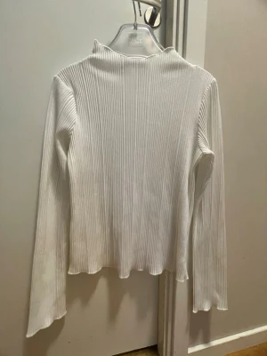 Vit ribbad polotopp från BikBok - Säljer en vit ribbad polotopp från BikBok i storlek XS. Toppen har lång ärm, hög krage och är tillverkad i stretchigt material som sitter snyggt på kroppen. Perfekt att styla med jeans eller kjol för en clean look.