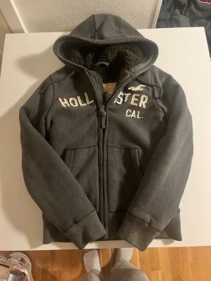 Mörkgrå hoodie från Hollister - Riktigt fet zip hoodie från Hollister fodrad i fint skick inga fel. Storlek M skulle säga M/L passar. Pris 800 kr 😁