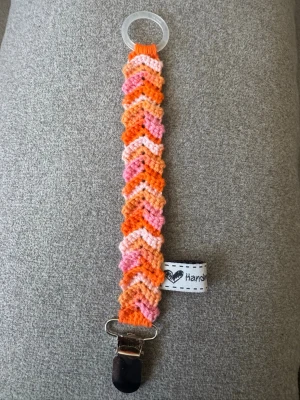 Virkad napphållare - Virkad, flerfärgad napphållare, i rosa och orangea toner. Virkad av mig i 100% bomullsgarn med metallclip och silikonring.  Mönsterskapare: animo.design