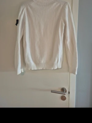 Vit stickad tröja i bomull från Stone island - Säljer en stilren vit stickad tröja med lång ärm, tillverkad i 100% bomull. Tröjan har ribbstickade muddar vid ärmslut och nederkant. Perfekt för dig som gillar klassiska och enkla plagg.