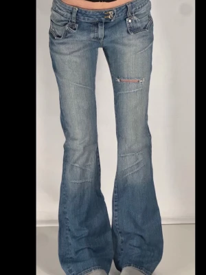 Blå bootcut jeans med slitning - Storlek= 38, S/M. Midjemått=40cm.     Innerbenslängden= 85cm. Midjehöjd=20cm. Inga defekter. Coola blå bootcut jeans med slitning på låret och snygga detaljer på fickorna. Jeansen har låg midja, klassisk femficksdesign och är tillverkade i denim med lätt tvättad look. Perfekt för dig som gillar en avslappnad och trendig stil.
