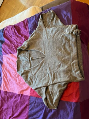 Grå stickad hoodie från Monrow - Säljer en yoga grå stickad halv hoodie från Monrow med avslappnad passform och halv huva. Tröjan har långa ärmar och dragsko i nederkanten för justerbar stil. Perfekt för en chill look och enkel att matcha med jeans eller leggings.