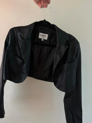 Svart cropped kavaj  - Snygg svart cropped kavaj med klassisk krage, två fickor framtill och knappdetalj.