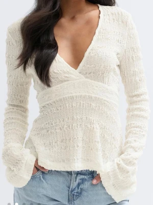 Vit omlottopp  - Säljer en vit omlottopp med v-ringning och långärmad design. Toppen har en ribbad struktur och är tillverkad i ett mjukt material som ger en skön känsla. Perfekt att styla med jeans eller kjol för en trendig look.
