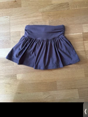 Mörkbrun kortkjol med volang - Säljer en söt mörkbrun kortkjol med bred midjeresår och volangig kjoldel samt insydda shorts. Kjolen är i mjukt bomullstyg och har en enkel, stilren look som passar till många olika outfits.