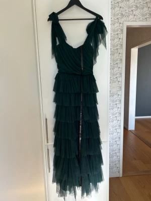 Mörkgrön balklänning med rosetter - Säljer en lång mörkgrön klänning med flera lager volanger och breda axelband som knyts i rosetter. 