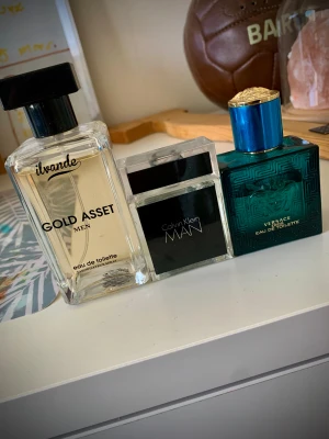 Herrparfymer från Versace, Calvin Klein & Ivande - Tre herrparfymer: Versace Eros i en turkosblå glasflaska med gulddetaljer, Calvin Klein MAN i en stilren svart och silverfärgad flaska samt Ivande Gold Asset Men i en transparent rektangulär flaska med svart lock. Alla är eau de toilette.