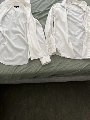 Klassisk vit skjorta i bomull - Säljer två klassiska vita skjorta från ”RIVER ISLAND” och ”THESE GLORY DAYS”i bomull. Skjortan har lång ärm, knappar framtill och en tidlös design som passar till allt. Perfekt basplagg för garderoben och enkel att styla till olika looks.