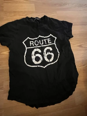 Svart shirt - Cool svart t-shirt med stort Route 66-tryck i vitt framtill. Klassisk rund hals och korta ärmar. Perfekt för dig som gillar retro och streetstyle. Passar till jeans eller shorts för en avslappnad look.