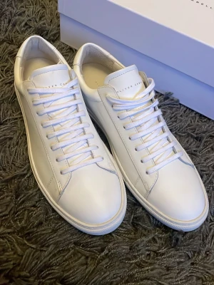 Vita låga sneakers från Oliver Cabell - Stilrena vita sneakers från Oliver Cabell i klassisk låg modell. Skorna är tillverkade i slätt läder med vita snören och diskret branding på plösen. Tidlös design med rund tå och vit sula som passar till det mesta. Perfekta för dig som gillar minimalistisk stil.