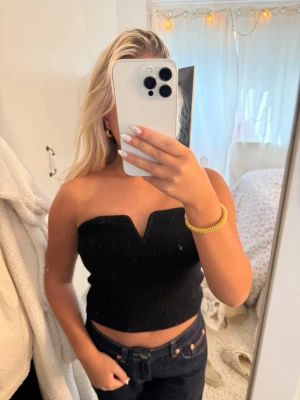 Svart stickad tubtopp - Säljer en svart stickad tubtopp med en snygg v-formad urringning. Toppen är croppad och sitter tight, perfekt till jeans eller kjol. Materialet är mjukt och stretchigt vilket gör den bekväm att bära. Enkel men trendig design som passar till många olika stilar.