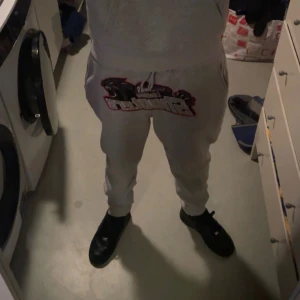 Grå mjukisbyxor Trapstar London Shooters - Säljer ett par grå mjukisbyxor från Trapstar med stort broderat London Shooters-motiv och svart panter på framsidan. Byxorna har snörning i midjan och ribbade muddar vid bensluten. Perfekt för chill och streetwear.