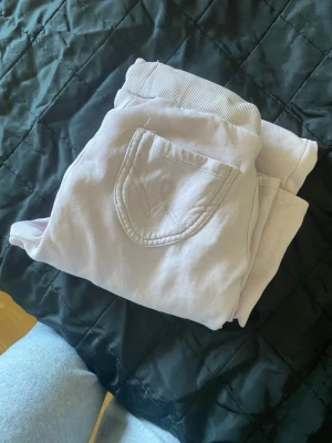 Ljusa rosa mjukisbyxor med fickor - Säljer ett par ljusa rosa mjukisbyxor med ribbad midja och snörning. Byxorna har en bakficka med broderad detalj och är tillverkade i mjukt bomullsmaterial. Perfekta för chill och avslappnade dagar.