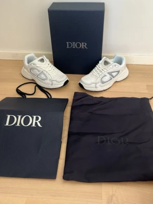 Vita B30 - Säljer ett par vita Doir B30 sneakers med grå detaljer och tydligt Doir-logo på sidan. Skorna har en chunky sula i vitt och svart, och är tillverkade i en mix av läder och mesh. Medföljer originalkartong, dustbag och shoppingbag.