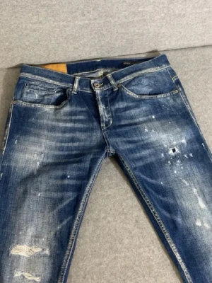 Blå Dondup Jeans - Säljer ett par blå jeans med coola slitningar och distressed detaljer. Jeansen har en klassisk femficksmodell, ljusa tvättade partier och små färgstänk för en trendig look. Perfekta för dig som gillar streetstyle och vill ha ett par unika jeans i garderoben.