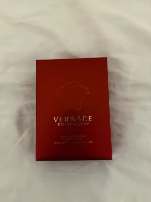 Versace Eros Flame Eau de Parfum - Versace Eros Flame Eau de Parfum i en elegant röd kartong med guldtext och Medusa-symbol. Förpackningen är stilren och lyxig, perfekt för dig som vill ha en exklusiv parfym från ett välkänt märke. Volymen är 100 ml.
