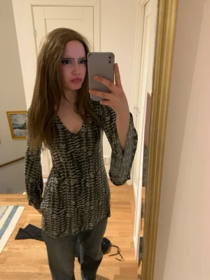 Zebramönstrad v-ringad blus - Säljer en zebramönstrad blus med v-ringning och långa, lätt utsvängda ärmar. Blusen har en loose passform och är gjord i ett tunt, skönt syntetmaterial. Perfekt för dig som gillar coola mönster och vill ha något som sticker ut.