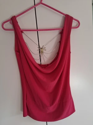 Rosa ärmlös topp med djup rygg - Cool rosa topp med djup, draperad rygg och ärmlös design. Materialet känns mjukt och stretchigt, perfekt för att sticka ut. Toppen har en snygg och enkel form som passar till många olika outfits.