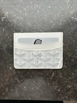 Korthållare - Säljer min otroligt eleganta plånbok från * i den eftertraktade vita färgen. En tidlös klassiker som kombinerar lyx med funktionalitet. Plånboken är tillverkad i * ikoniska handmålade Goyardine-canvas med detaljer i högkvalitativt läder.