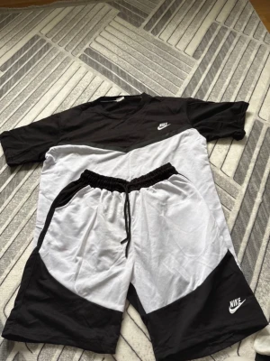 Svartvit t-shirt  Nike - Snygg svartvit t-shirt Nike med logga på bröstet. T-shirten har en rak passform och är kortärmad. Tillverkad i mjukt bomullsmaterial som känns skönt mot huden. Perfekt för en sportig och avslappnad stil.not real nike