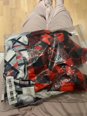 3-pack mönstrade pyjamasshorts - Säljer ett 3-pack pyjamasshorts i olika rutiga mönster. Färgerna är röd, vit, svart och blå i olika kombinationer. Shortsen har bred resår i midjan och är tillverkade i mjukt och stretchigt material för skön passform. De är i nytt skick men utan prislapp. Aldrig använda!