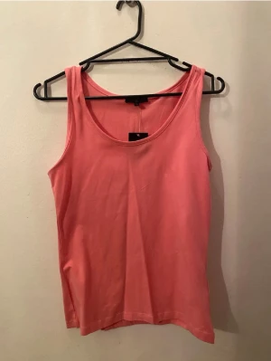 Cerise linnetopp från H&M - Snygg cerise linnetopp från H&M i mjuk bomull. Enkel och stilren design med rund halsringning och ärmlös passform. Perfekt att matcha med jeans eller kjol för en fräsch look.