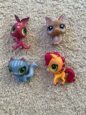 Littlest Pet Shop figurer 4-pack - Fyra färgglada Littlest Pet Shop figurer: en vinröd kanin, en beige/brun katt, en blå katt och en orange häst med rosa man. Alla har stora gröna ögon och detaljerade ansikten. Perfekta för samlare eller som leksaker till barnrummet.