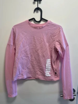 Rosa långärmad tröja från Puma - Snygg rosa långärmad tröja från Puma med vit logga tryckt på framsidan. Tröjan har rund halsringning och är gjord i mjukt bomullsmaterial. Perfekt för en avslappnad och sportig stil.