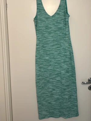 Grön ribbad långklänning - Säljer en grön ribbad långklänning med v-ringning och ärmlös design. Klänningen har ett diskret mönster och är perfekt för dig som gillar en enkel och stilren look. Materialet är mjukt och stretchigt, vilket gör den bekväm att bära.