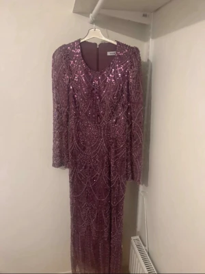 Lila glittrig långklänning med paljetter - Säljer en fantastisk långklänning från Turkiet. med glittriga paljetter och långärmad design. Klänningen har rund halsringning och ett vackert mönster av paljetter över hela plagget. Perfekt för dig som vill sticka ut på bal eller fest.